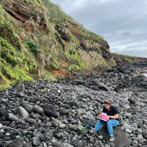 A member of the team sits on a rock on the sea shore
