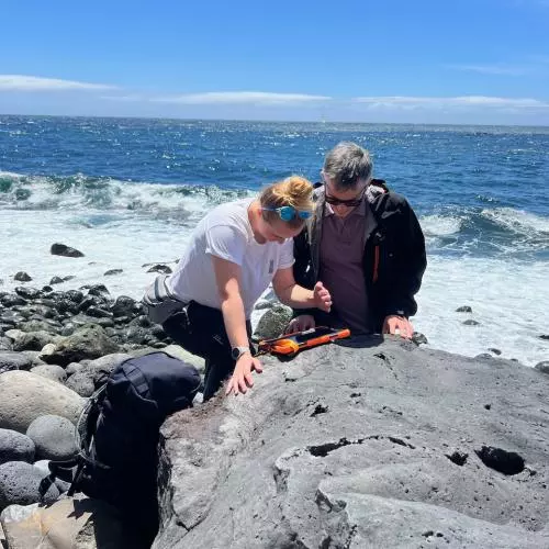 Two people on the sea shore looking at rocks