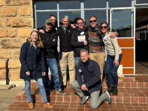 A photo of peter mitchell surrounded by six current and former students